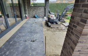 Grote keramische tegels onder een overkapping, minigraver op de achtergrond