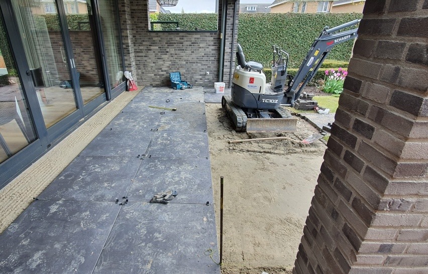 Grote keramische tegels onder een overkapping, minigraver op de achtergrond